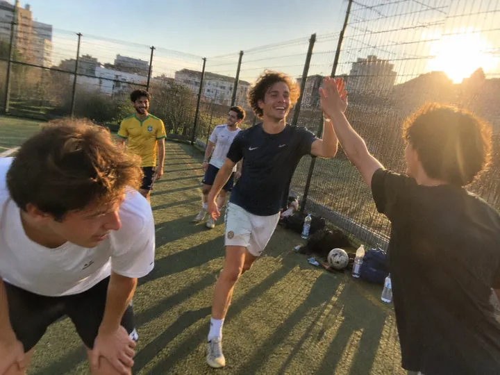 Friends high-fiving on a small city football pitch at sunset